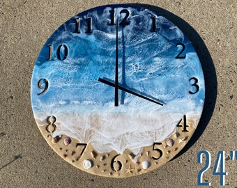 Può includere: Un orologio in resina da 61 cm di diametro con una scena di spiaggia. Il quadrante dell'orologio è blu e bianco con un design a onde. I numeri sono neri e le lancette sono nere e bianche. La parte inferiore del quadrante dell'orologio è una spiaggia sabbiosa con conchiglie e una stella marina.