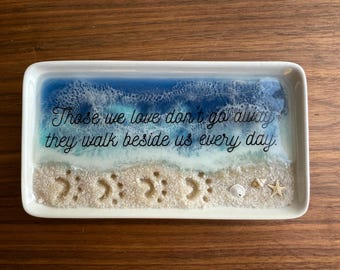 May include: White ceramic tray with a blue and white resin ocean scene. The tray has the quote "Those we love don't go away, they walk beside us every day." and seashells and a starfish.