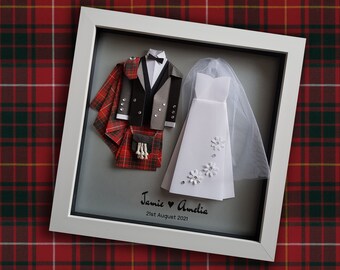 May include: A framed paper art piece depicting a wedding couple. The groom is wearing a kilt and the bride is wearing a white dress. The frame has a gray background with the text "Jamie ♥ Amelia 21st August 2021".
