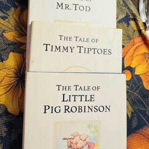 Op de afbeelding: Een stapel Beatrix Potter-boeken, waaronder "The Tale of Samuel Whiskers", "The Tale of Mr. Tod", "The Tale of Timmy Tiptoes" en "The Tale of Little Pig Robinson". De omslag van "Little Pig Robinson" toont een varken in een stoel.