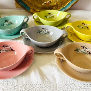 May include: A collection of six vintage ceramic soup bowls and saucers in various pastel colors: teal, yellow, pink, gray, and tan. Each bowl has two handles and a decorative floral design.