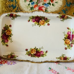 Puede incluir: Una bandeja de servir de porcelana blanca con un borde dorado y un diseño floral con rosas rojas, amarillas y rosas. La bandeja tiene un borde festoneado y es perfecta para servir té o aperitivos.