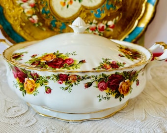 May include: White ceramic serving dish with a lid, adorned with a floral rose pattern in shades of red, yellow, and green. The dish has gold trim and handles, and a decorative finial on the lid. A vintage-style piece.