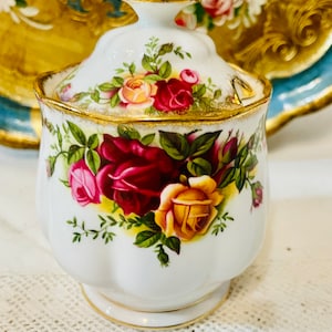 Peut inclure: Un sucrier en céramique blanche avec un couvercle, orné d'un motif floral de roses rouges, roses et jaunes et de feuilles vertes. Le bord et la poignée sont dorés. Le bol a une forme festonnée.