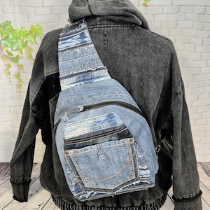 Könnte beinhalten: Eine blaue Jeans-Umhängetasche mit schwarzem Reißverschluss und einer Tasche aus recycelten Jeans. Die Tasche wird über der Schulter und über der Brust getragen. Die Tasche besteht aus mehreren Jeans-Teilen.