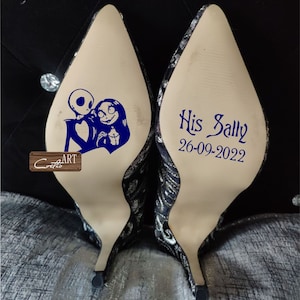 May include: A pair of white high-heeled shoes with a black and silver patterned design. One shoe has a blue graphic of Jack and Sally from The Nightmare Before Christmas. The other shoe has the text "His Sally 26-09-2022" in blue.