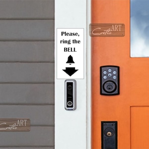 Könnte beinhalten: Ein weißes Schild mit schwarzem Text, auf dem "Please, ring the BELL" steht, mit einem schwarzen Glockensymbol und einem schwarzen Pfeil, der nach unten zeigt. Das Schild ist an einem weißen Türrahmen neben einer schwarzen Türklingel angebracht.