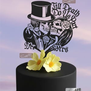 May include: A black cake topper featuring a skeleton couple in a top hat and veil, with the text Till Death Do Us Part and Mr Mrs. The design includes roses and is placed on a smooth black cake decorated with two yellow flowers and a gold ribbon.