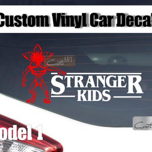 May include: Custom vinyl car decal featuring a red Demogorgon graphic and the text "Stranger Kids" in white. The decal is displayed on a car window, with the text "Model 1" visible below.