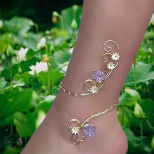 Könnte beinhalten: Ein zartes Fußkettchen aus Gold und Silber mit floralem Design. Das Armband zeigt lila und weiße Blumen mit goldenen Akzenten.
