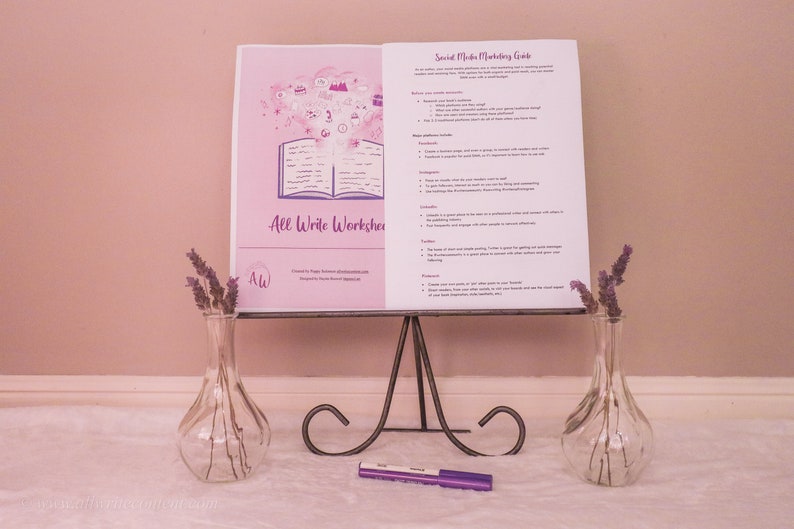 May include: A white booklet with the title "All Write Workshop" and a purple illustration of an open book with a cloud of ideas above it. The booklet is on a black metal stand with a purple marker on a white surface. Two clear glass vases with purple flowers are on either side of the stand.