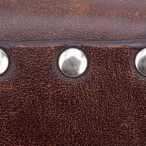 May include: Close-up of brown leather with three silver metal rivets.