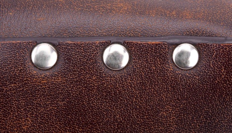 May include: Close-up of brown leather with three silver metal rivets.