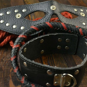 May include: A black leather mask with silver studs, a black leather choker with silver studs, and a black and red braided leather whip.