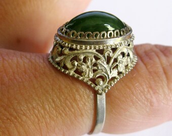 Pode incluir: Um anel de prata com uma gema verde engastada em um design filigranado.