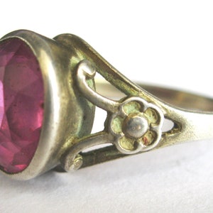 May include: A silver ring featuring a pink gemstone set in a bezel setting. The ring band has a delicate floral design.