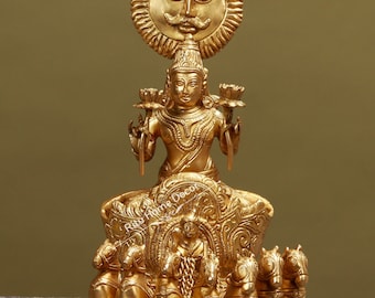 May include: A gold-colored statue of the Hindu deity Surya, the Sun God, riding a chariot pulled by seven horses. The statue is intricately detailed and features a sun halo above Surya's head.