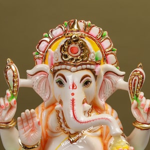 Puede incluir: Estatua de mármol blanco de la deidad hindú Ganesha, con una corona colorida y detalles intrincados. La estatua está representada con una trompa, orejas grandes y cuatro brazos, sosteniendo varios objetos.