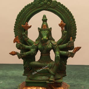 May include: A green and gold statue of a deity with multiple arms and a pig-like face, seated in a meditative pose. The statue is set against a neutral background and features intricate details and ornate design elements.
