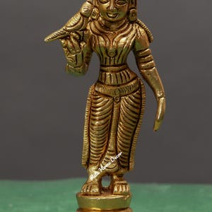 May include: A gold-colored metal statue of a deity with a bird perched on its arm. The statue is standing on a tiered base with intricate details.