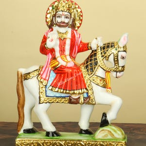 May include: A detailed statue of a figure riding a white horse. The figure wears a red and gold robe, a gold crown, and a halo. The horse has gold accents on its bridle and saddle. The base is gold with a green and white landscape.