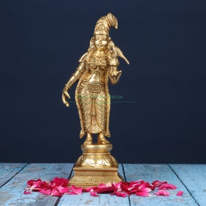 May include: A gold-colored metal statue of a Hindu deity, standing on a pedestal with a bird perched on her shoulder. The statue is intricately detailed and has a traditional Indian design.