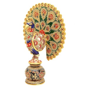 May include: A decorative peacock figurine with a detailed design. The peacock has a blue head, red accents, and a green and gold tail. The base is black with red and gold floral patterns.