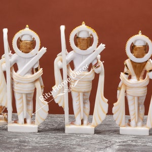 May include: Four white marble statues of Hindu deities with gold accents. The statues are standing and are arranged in a row. The statues are all facing the same direction. The statues are all wearing traditional Indian clothing.