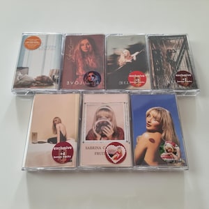 May include: A collection of eight cassette tapes featuring various artists. The tapes are in clear plastic cases with colorful artwork and text. Some of the tapes have stickers that say "exclusive" and "bonus tracks".