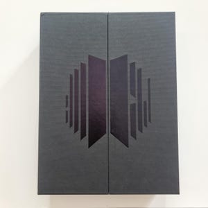 Puede incluir: Una caja negra con un gráfico estilizado de líneas verticales que forman un diseño simétrico. La caja está cerrada y tiene una superficie lisa.