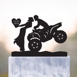 Puede incluir: Topper de pastel en silueta negra de una pareja besándose en un ATV. La mujer sostiene un corazón con la fecha "15.07.2019" en él.