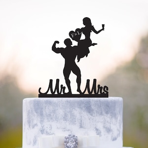 May include: Black silhouette cake topper of a bride sitting on the shoulders of a groom with a heart that says "F&L" above them. The topper says "Mr. Mrs."