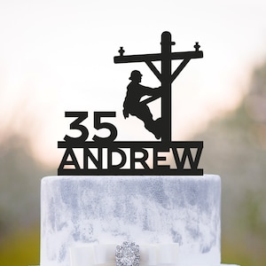 Op de afbeelding: Zwarte silhouet caketopper van een persoon die op een elektriciteitspaal klimt met het nummer 35 en de naam Andrew eronder.
