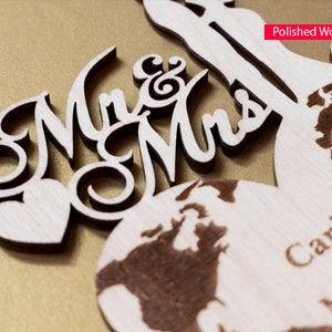 May include: Wooden wedding sign with the words "Mr & Mrs" in a decorative font. The sign features a heart and a world map with the names "Carina & Mic" engraved on it. The sign is made of polished wood.