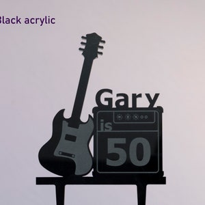 May include: Black acrylic cake topper featuring a silhouette of a guitar and amplifier with the text "Gary is 50".