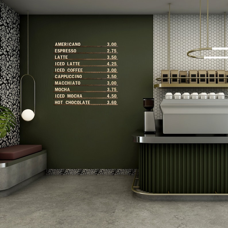 Op de afbeelding: Een groene muur met een houten bord waarop koffiedrankjes en prijzen staan vermeld. Het bord toont: Americano &euro;3,00, Espresso &euro;2,75, Latte &euro;3,50, IJslatte &euro;4,25, Iced Coffee &euro;3,00, Cappuccino &euro;3,50, Macchiato &euro;3,00, Mocha &euro;3,75, Iced Mocha &euro;4,50, Warme Chocolademelk &euro;3,60. Een zilveren koffiemachine staat op een toonbank met een groene en gouden rand.