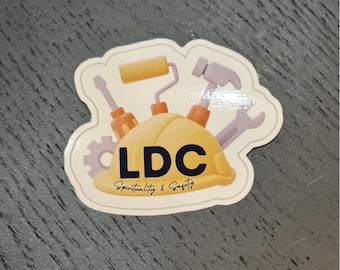 Puede incluir: Una pegatina blanca con un casco amarillo, una llave inglesa, un destornillador, un rodillo de pintura y el texto "LDC Espiritualidad y Seguridad".