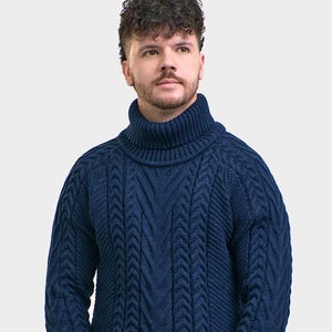 Può includere: Un maglione a trecce blu scuro caratterizzato da un prominente collo alto a coste, maniche lunghe con polsini a coste e un motivo verticale testurizzato sul davanti. Il capo è abbinato a un paio di jeans in denim grigio scuro coordinati.