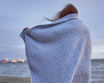 May include: A person wearing grey pants and a blue and white patterned blanket on a sandy beach.