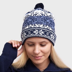 May include: A blue and white knitted beanie with a pom pom on top. The beanie has a snowflake pattern.