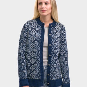 May include: A navy blue cardigan with a geometric snowflake pattern in light gray. The cardigan has a round neckline, long sleeves, and a button-up front. The cuffs and trim are solid navy blue.