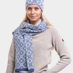 May include: A blue and white patterned knit beanie and matching scarf. The beanie has a diamond pattern with snowflakes. The scarf is a long rectangle with a similar pattern.