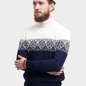 May include: A white turtleneck sweater with a blue and white snowflake pattern. The sweater has long sleeves and a ribbed collar.