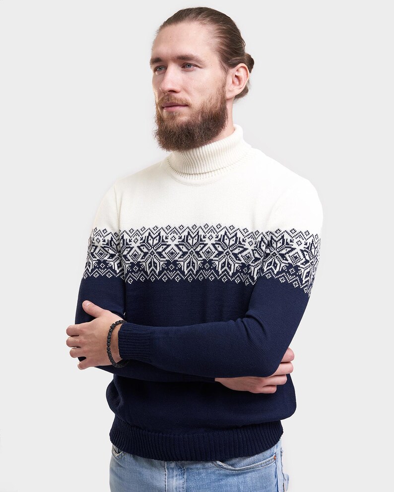 May include: A white turtleneck sweater with a blue and white snowflake pattern. The sweater has long sleeves and a ribbed collar.