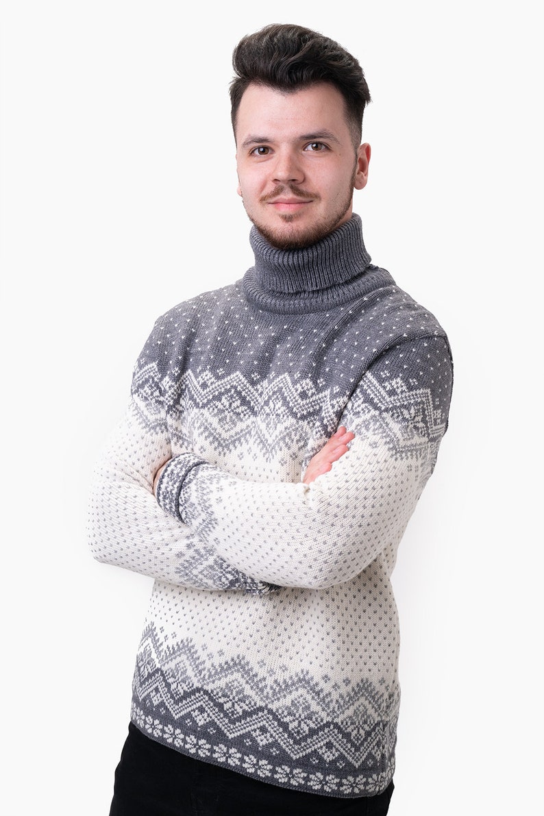 Peut inclure: Un pull &agrave; col roul&eacute; gris et blanc &agrave; motifs avec un design en jacquard. Le pull est pli&eacute; et pr&eacute;sent&eacute; sur un fond blanc.