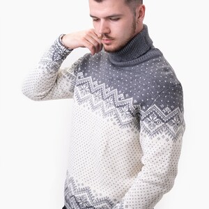 Peut inclure: Un pull &agrave; col roul&eacute; gris et blanc &agrave; motif nordique. Le pull est en tissu tricot&eacute; doux.