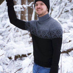 May include: A man wearing a black knit hat and a black and gray sweater with a snowflake pattern. He is wearing blue jeans and black gloves. The man is standing in a snowy forest.