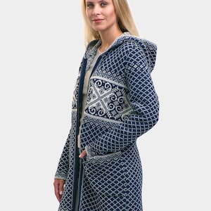 Puede incluir: Cárdigan largo con capucha en azul marino y blanco. El suéter presenta un patrón de diamantes y un diseño decorativo en la parte superior del pecho. Tiene cremallera completa y bolsillos.