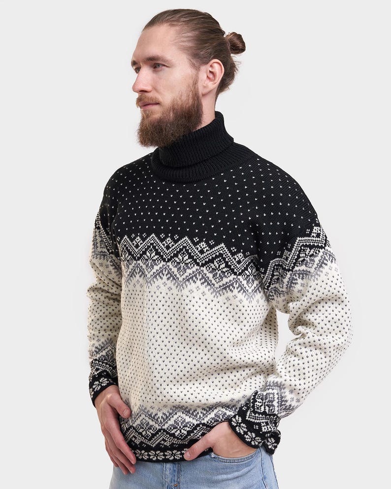 Peut inclure: Un pull &agrave; col roul&eacute; noir et blanc &agrave; motifs. Le pull est noir avec des motifs g&eacute;om&eacute;triques blancs et une bande blanche sur la poitrine.