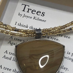 May include: A necklace with a triangular pendant made of brown agate with a silver trim. The pendant is surrounded by a triple strand of brown and gold beads. The necklace is accompanied by a card with the poem "Trees" by Joyce Kilmer.